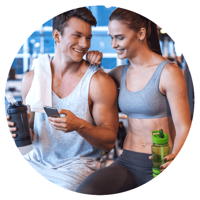 A man and woman are in a gym setting smiling while they look a their phones
